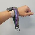 Load image into Gallery viewer, Rainbow metallic vegan leather key fob on a person's wrist.
