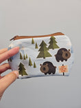 Load image into Gallery viewer, Hand holding a mini zipper pouch that has bears and trees on it against a light blue wall.
