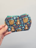 Load image into Gallery viewer, Hand holding a mini zipper pouch against a light gray wall with sloths on it.
