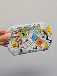 Load image into Gallery viewer, Hand holding a Looney Tunes themed zipper pouch against a gray wall.
