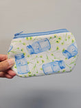 Load image into Gallery viewer, A hand holding a small zippered pouch with a white background, blue mason jar print, and small yellow flowers, against a plain gray wall.
