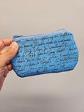 Load image into Gallery viewer, A hand holding a small zippered pouch with a blue background and black cursive script print, set against a plain light gray background.
