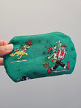 Load image into Gallery viewer, A hand holding a green zippered pouch featuring a festive Christmas cartoon print with Goofy, Pluto, and a nutcracker character against a plain light gray background.
