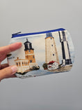 Load image into Gallery viewer, A hand holding a zippered pouch with a printed lighthouse design on a light gray background.
