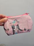 Load image into Gallery viewer, A hand holding a light pink zippered pouch decorated with a gothic girl illustration, featuring a floral crown, black hair, and spider motifs, set against a plain gray background.
