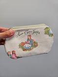 Load image into Gallery viewer, A hand holding a small zippered pouch featuring an Anne of Green Gables illustration and text on a plain gray background.
