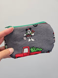Load image into Gallery viewer, A hand holding a gray zippered pouch with a Mickey Mouse Christmas print, featuring a red truck carrying a Christmas tree and a green zipper trim.
