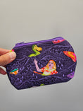 Load image into Gallery viewer, A hand holding a small zippered pouch with a purple background and a whimsical illustration of a woman in a raft with a green duck and colorful fish.
