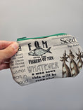Load image into Gallery viewer, A hand holding a small zippered pouch with a vintage-style seed and fish illustration print. The pouch has a light gray background with black text and graphics, a green zipper, and is shown against a plain gray background.
