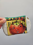 Load image into Gallery viewer, A hand holding a small zippered pouch with a vintage-style printed design featuring a red tomato face and the words 'GARDEN PATCH'. The pouch has a green zipper and a white fabric base.
