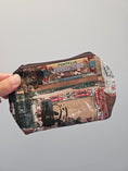 Load image into Gallery viewer, A hand holding a small zippered pouch with a vintage-style collage print featuring postmarks, stamps, and text.
