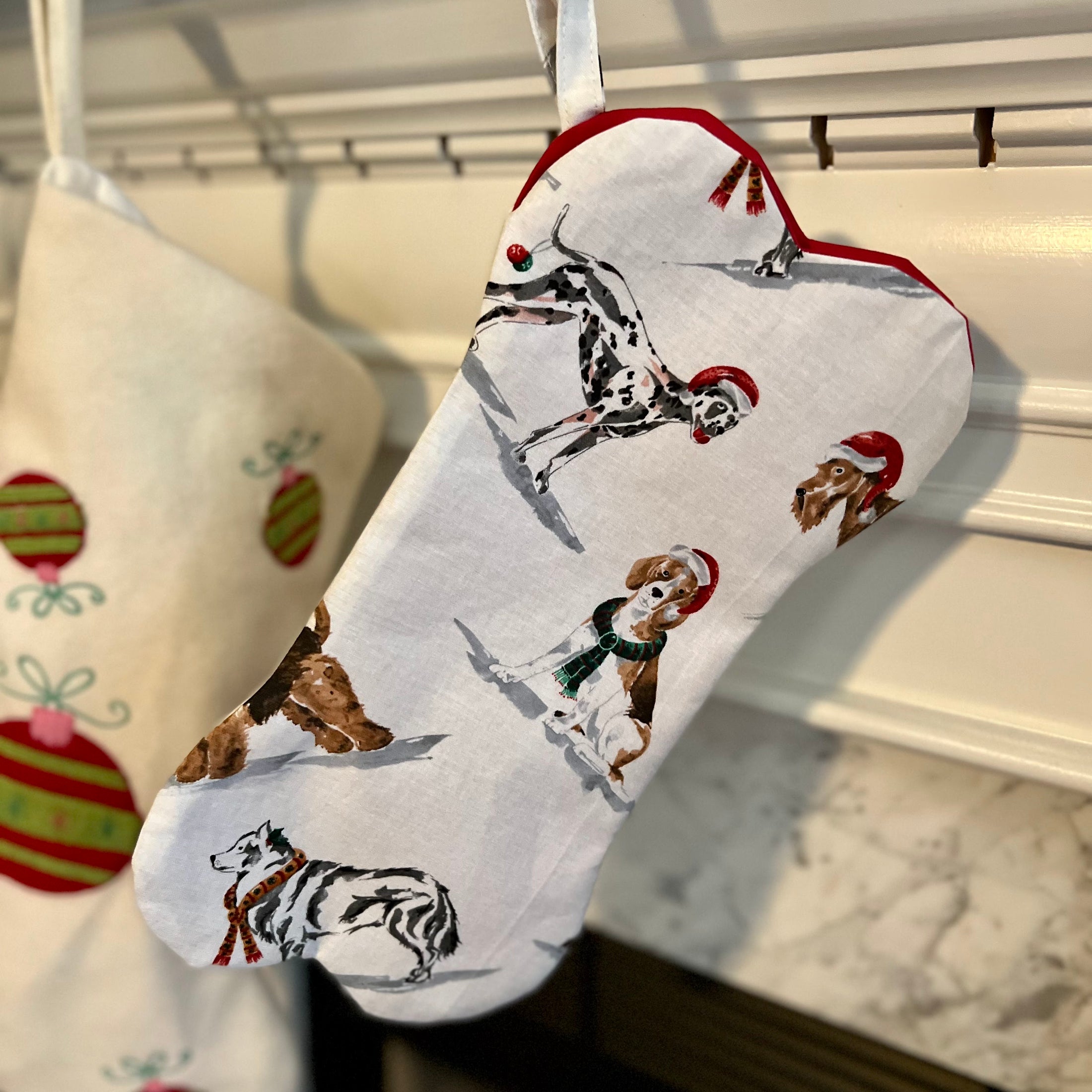 Bone shaped Christmas stocking for dogs hanging on a mantle with a red interior.