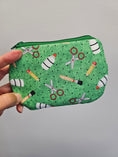 Load image into Gallery viewer, Hand holding a green zipper pouch with school supplies on it against a light gray wall.
