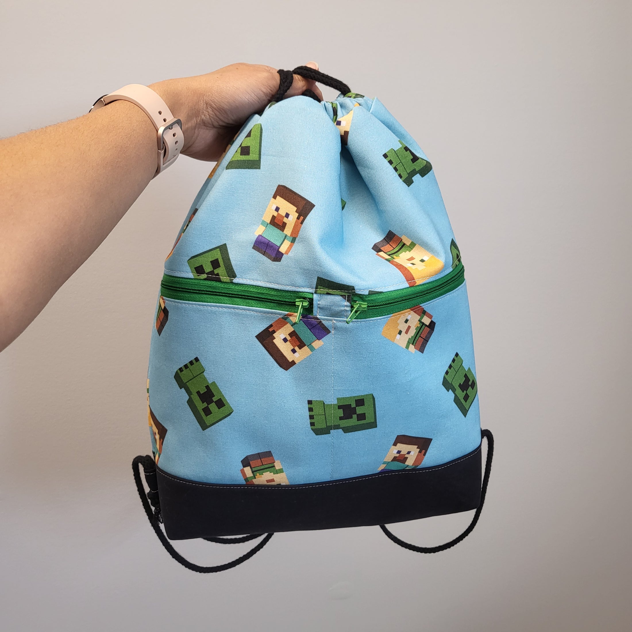 Minecraft inspired drawstring backpack with 2 exterior zipper pockets and black bottom. 