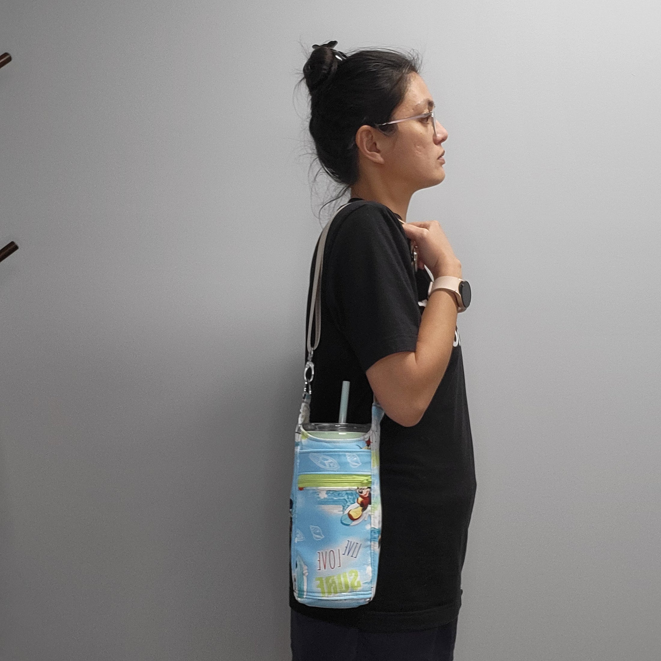 Person wearing the surfing mickey drink carrier bag on their shoulder with a drink in it. 