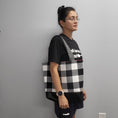 Load image into Gallery viewer, Person wearing the black and white flannel tote bag.
