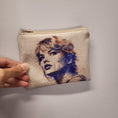 Load image into Gallery viewer, Front of the Swiftie zipper pouch showing a sketched image of Taylor Swift on a beige background. 
