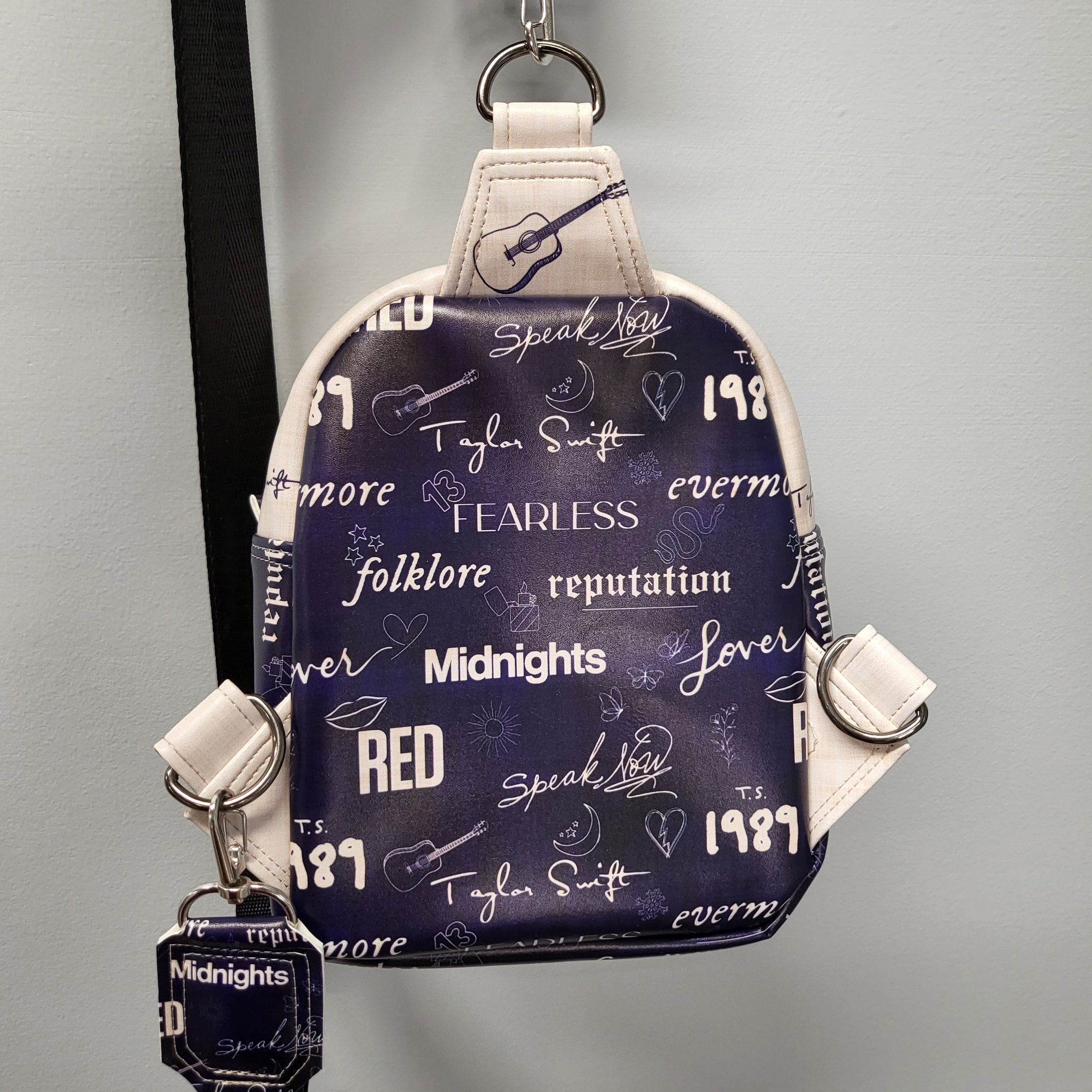 Back of the Swiftie sling bag that is dark blue with album titles in white. 