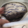 Load image into Gallery viewer, Waterproof canvas interior of the Swiftie sling bag that is beige with album titles in dark blue.
