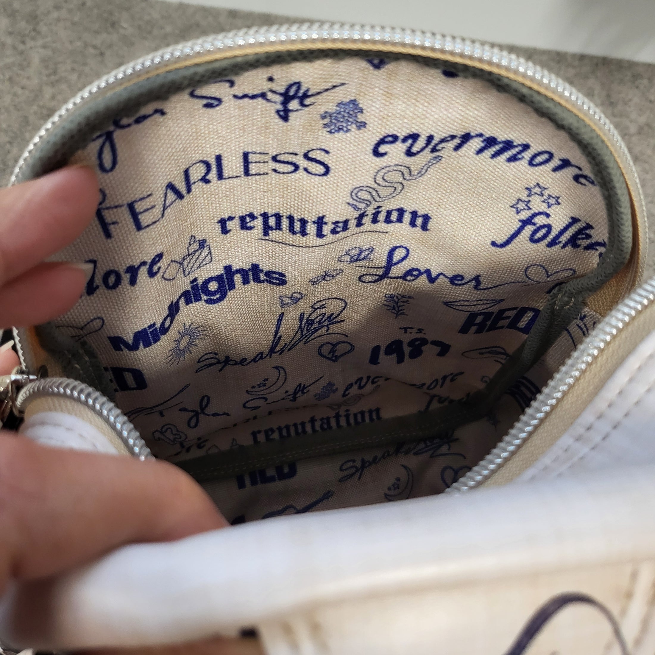 Waterproof canvas interior of the Swiftie sling bag that is beige with album titles in dark blue.
