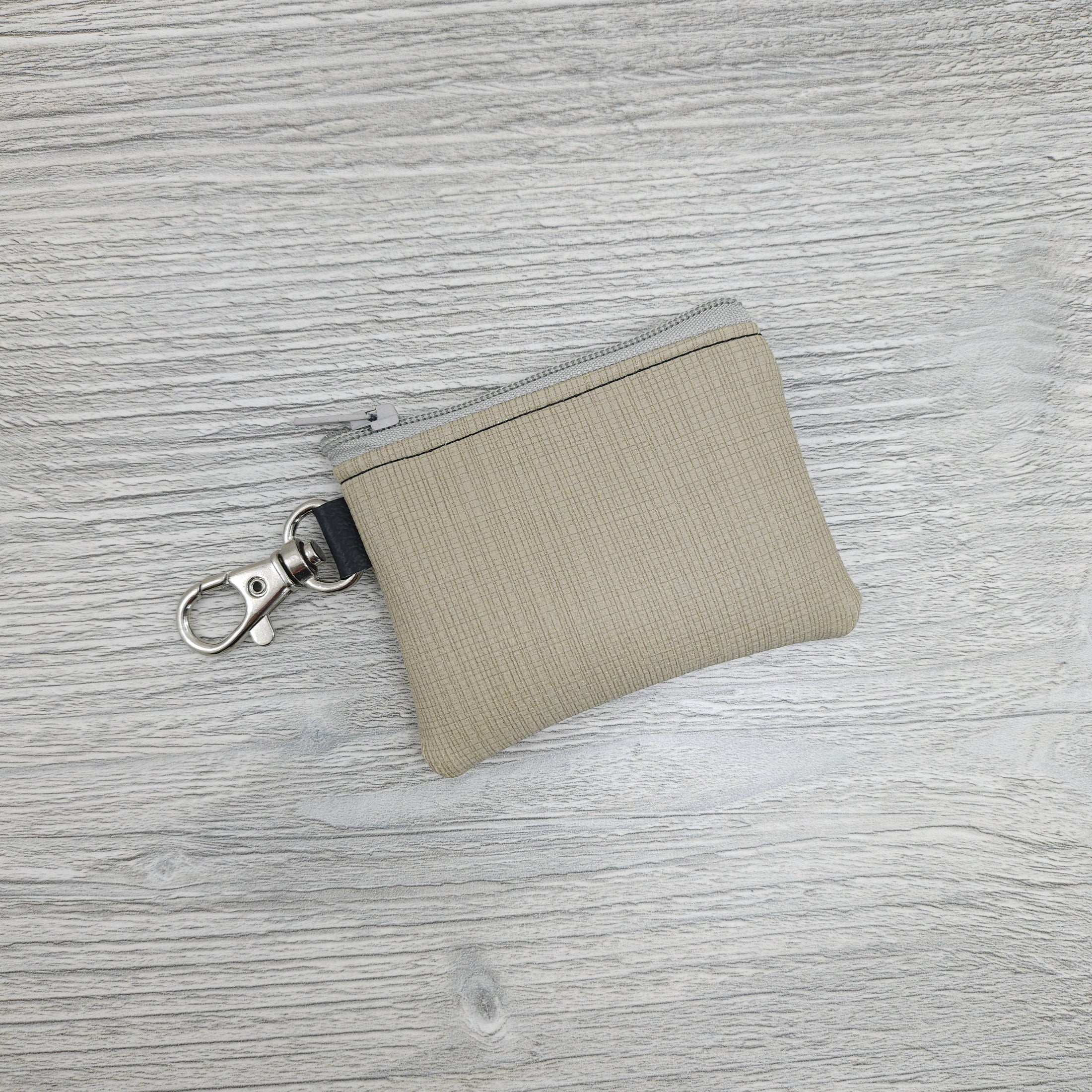 Mini beige, vinyl zipper pouch to hold small items like coin or cash and can be attached to key ring or purse.