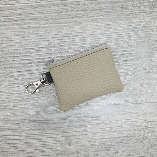 Mini beige, vinyl zipper pouch to hold small items like coin or cash and can be attached to key ring or purse.