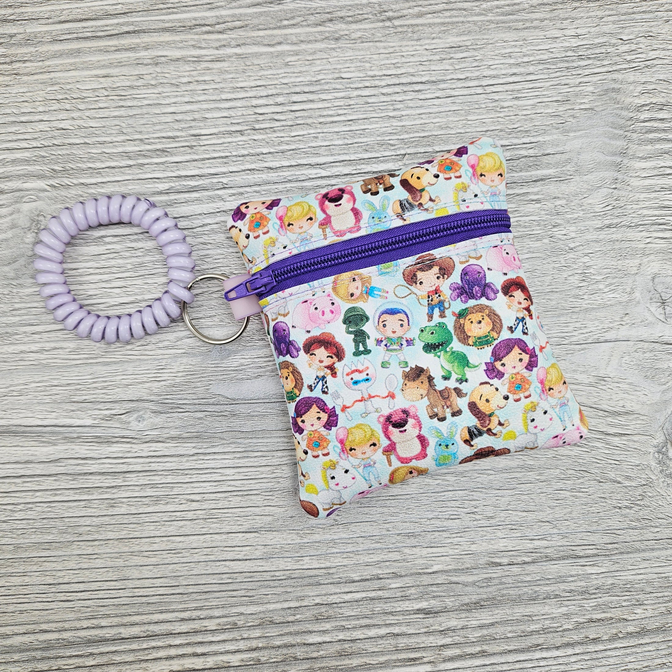 Mini vinyl zipper pouch featuring disney characters with a stretchy bracelet so you can wear it on your wrist. 