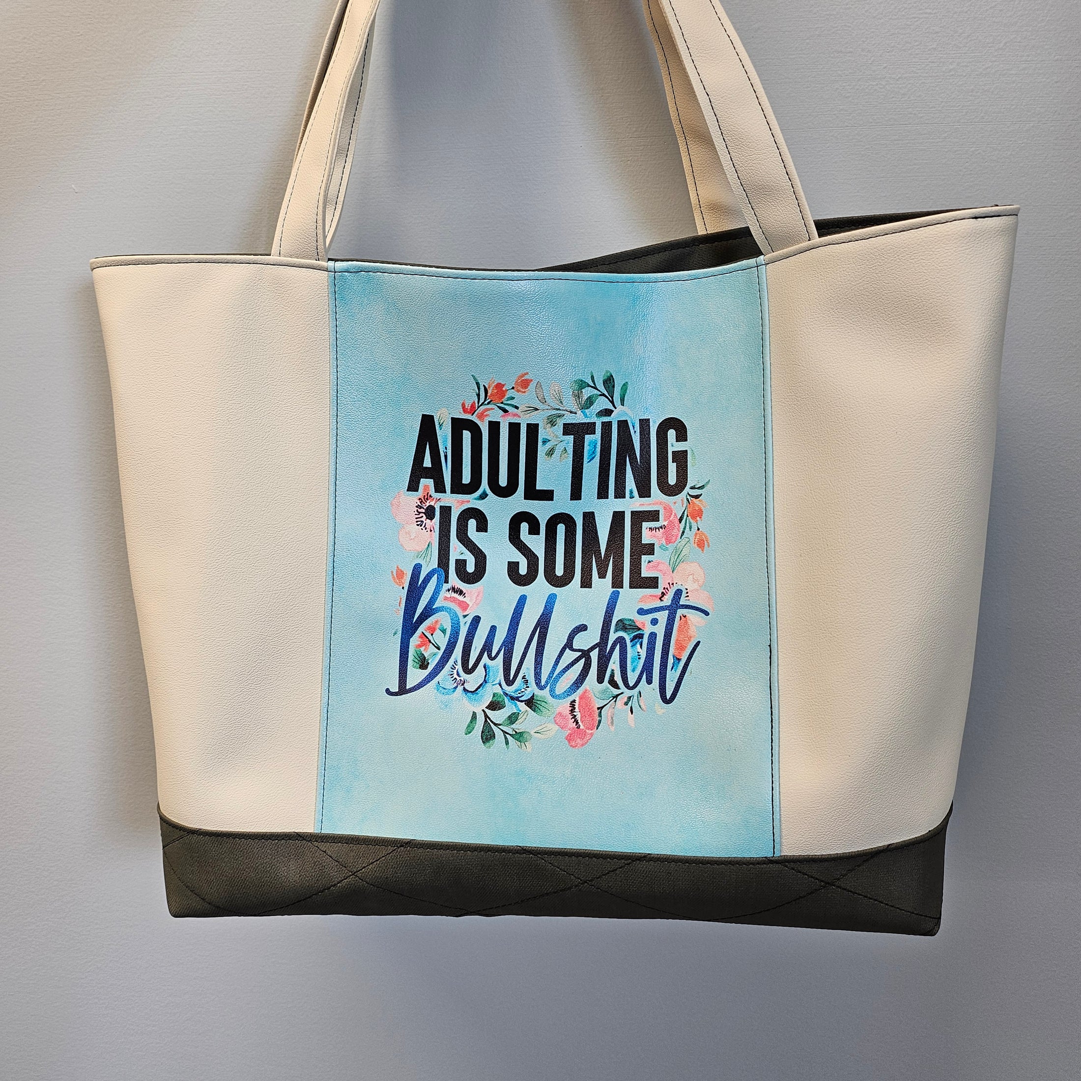 Bag with text 'ADULTING IS SOME B****H' on a light blue background