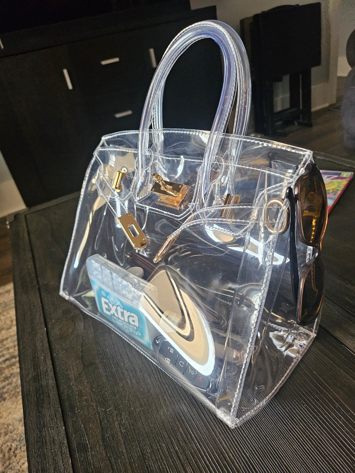 Clear birkin bag sitting on a dark brown table.