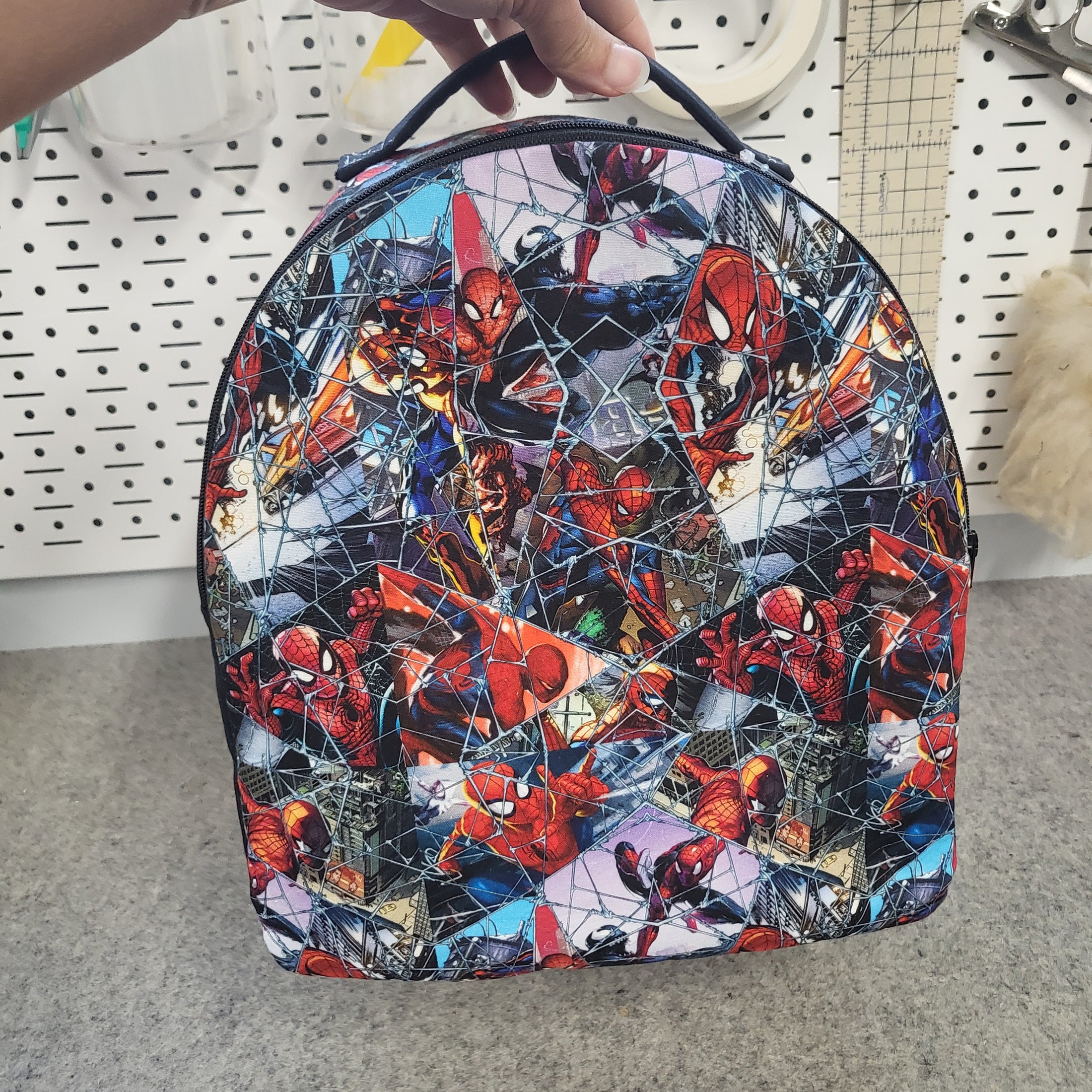 Hand holding up a spiderman backpack. 