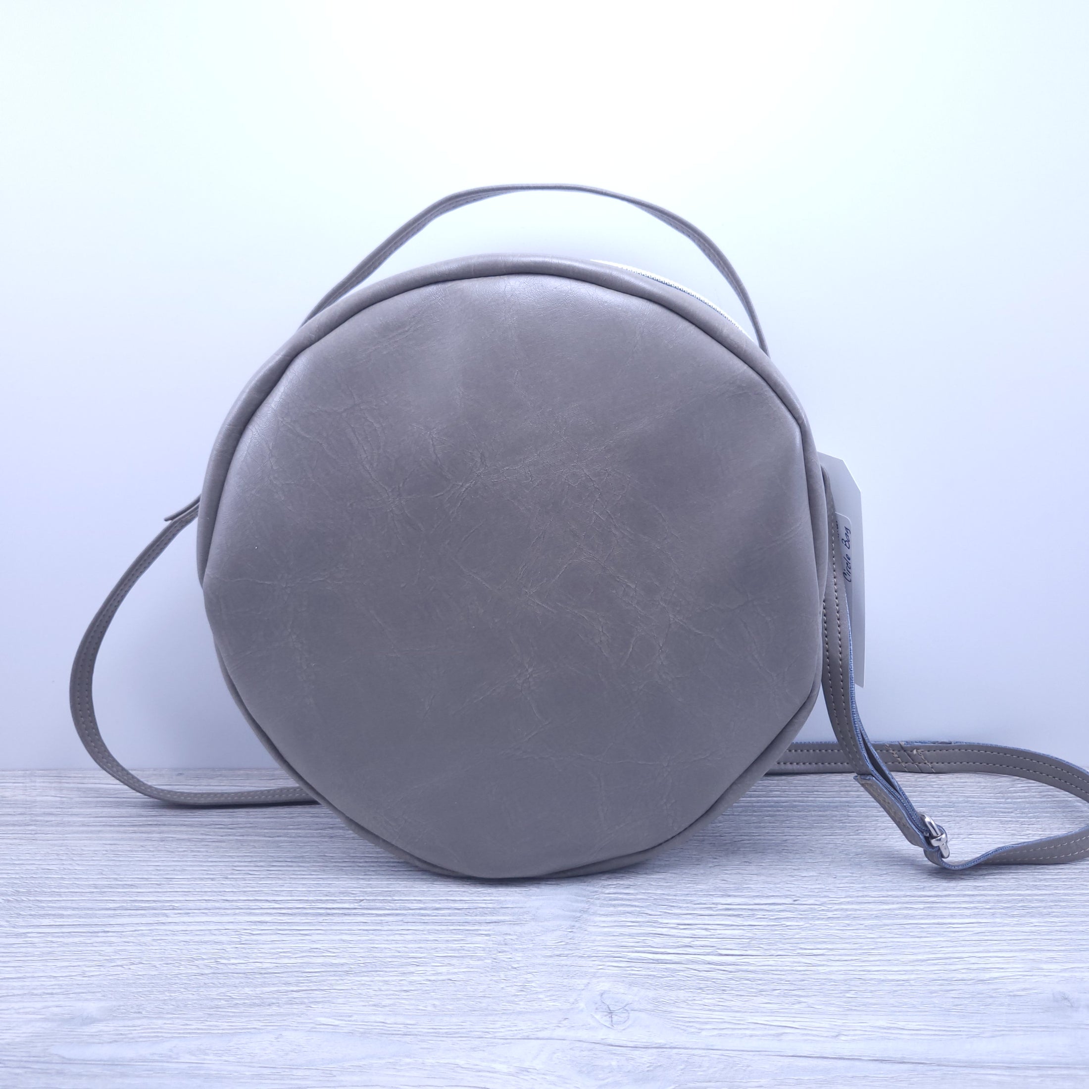 Front of taupe faux leather round purse. 